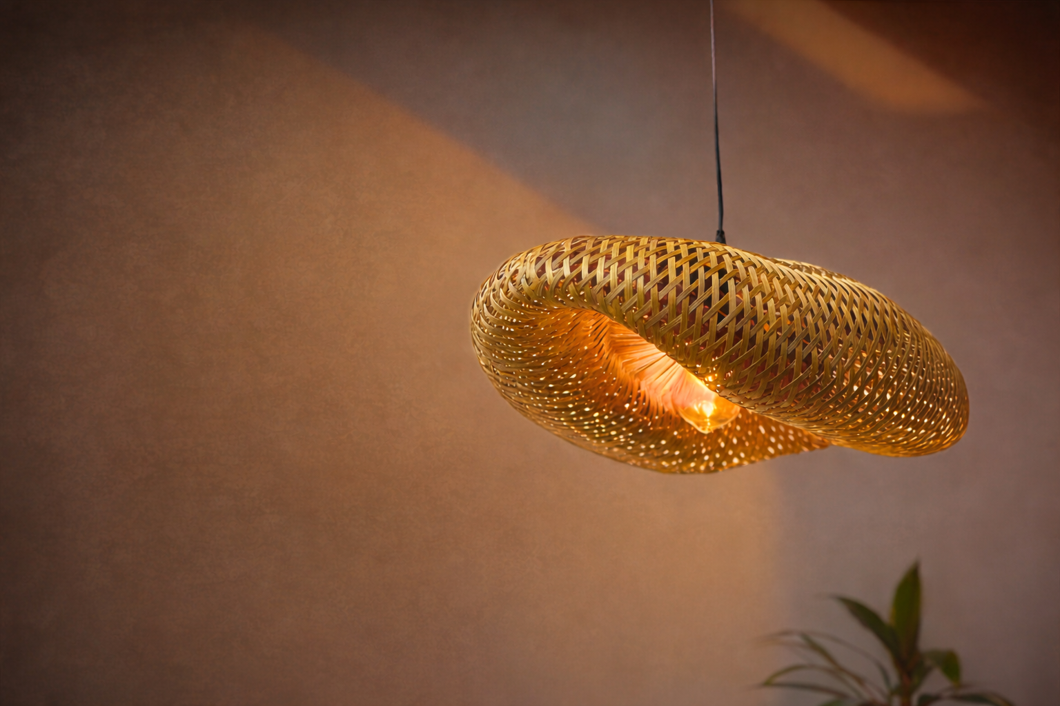 Woven pendant light hanging against a neutral wall with a plant in the corner