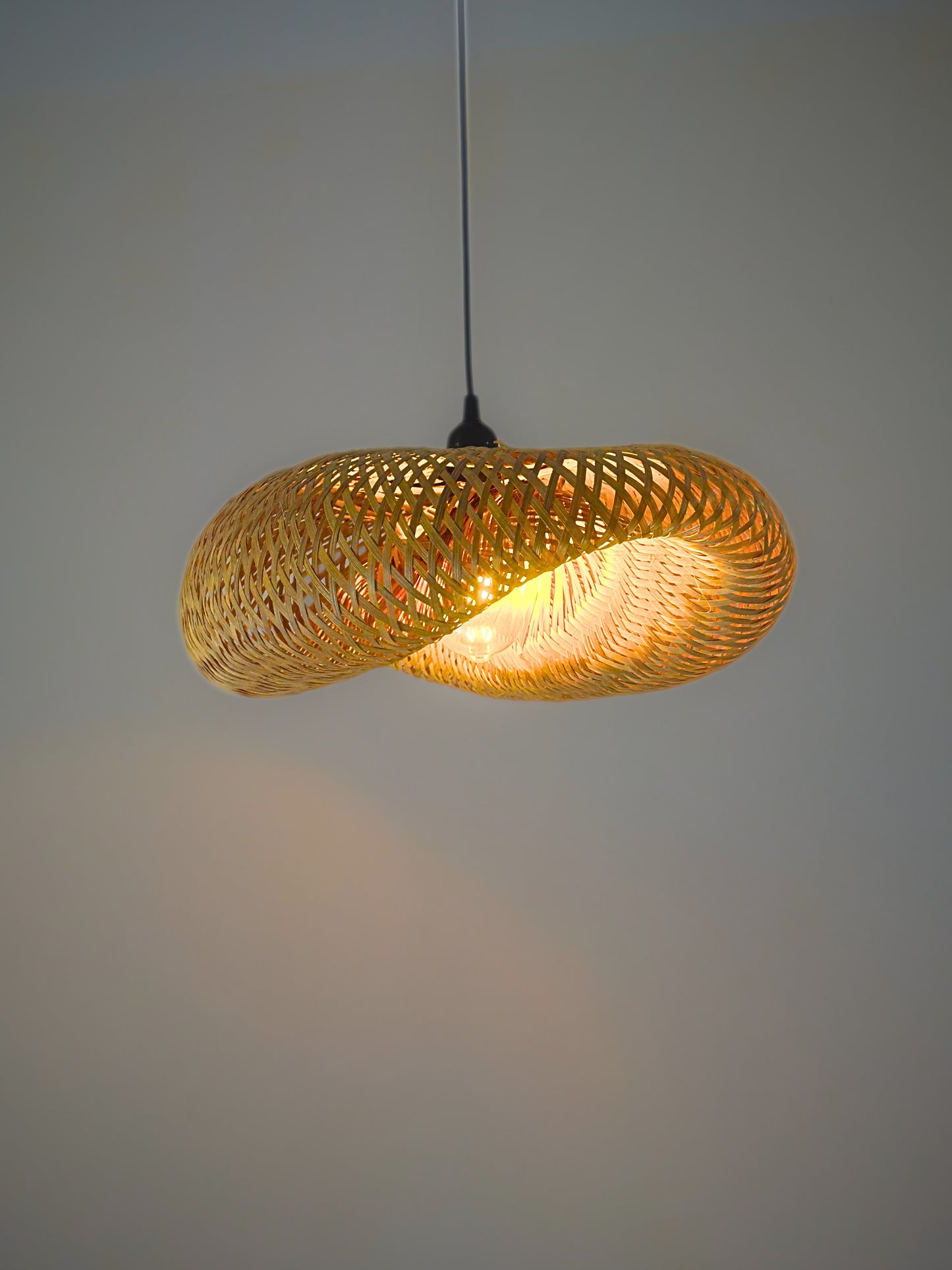 Woven pendant light with a warm glow on a plain background