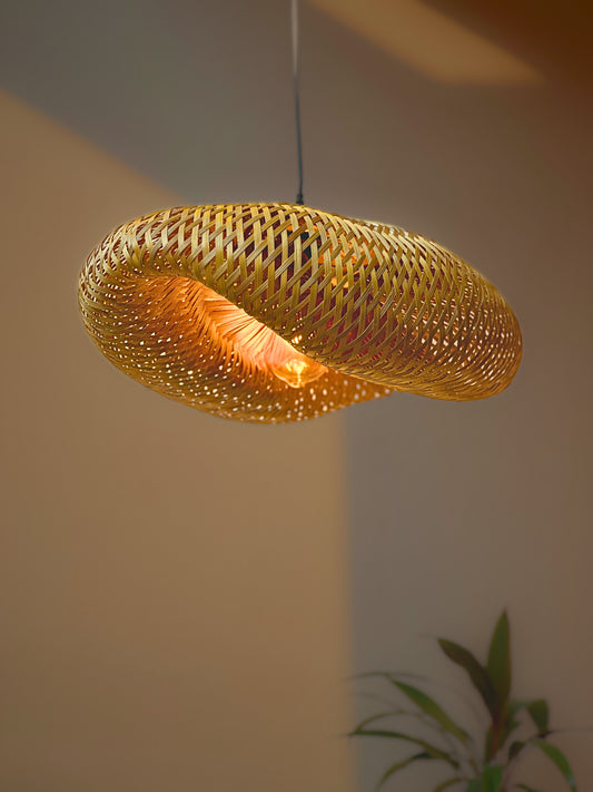 Woven pendant light hanging against a neutral wall with a plant in the corner.